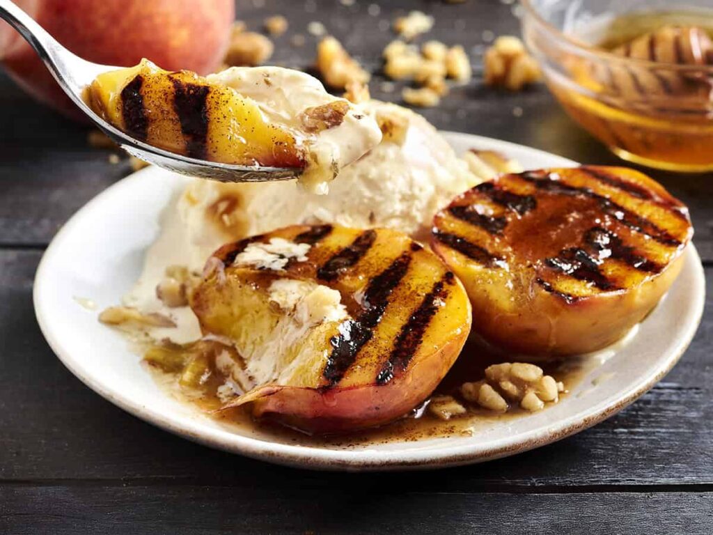 Side view of a plate of grilled peaches and cream with a spoon taking some.