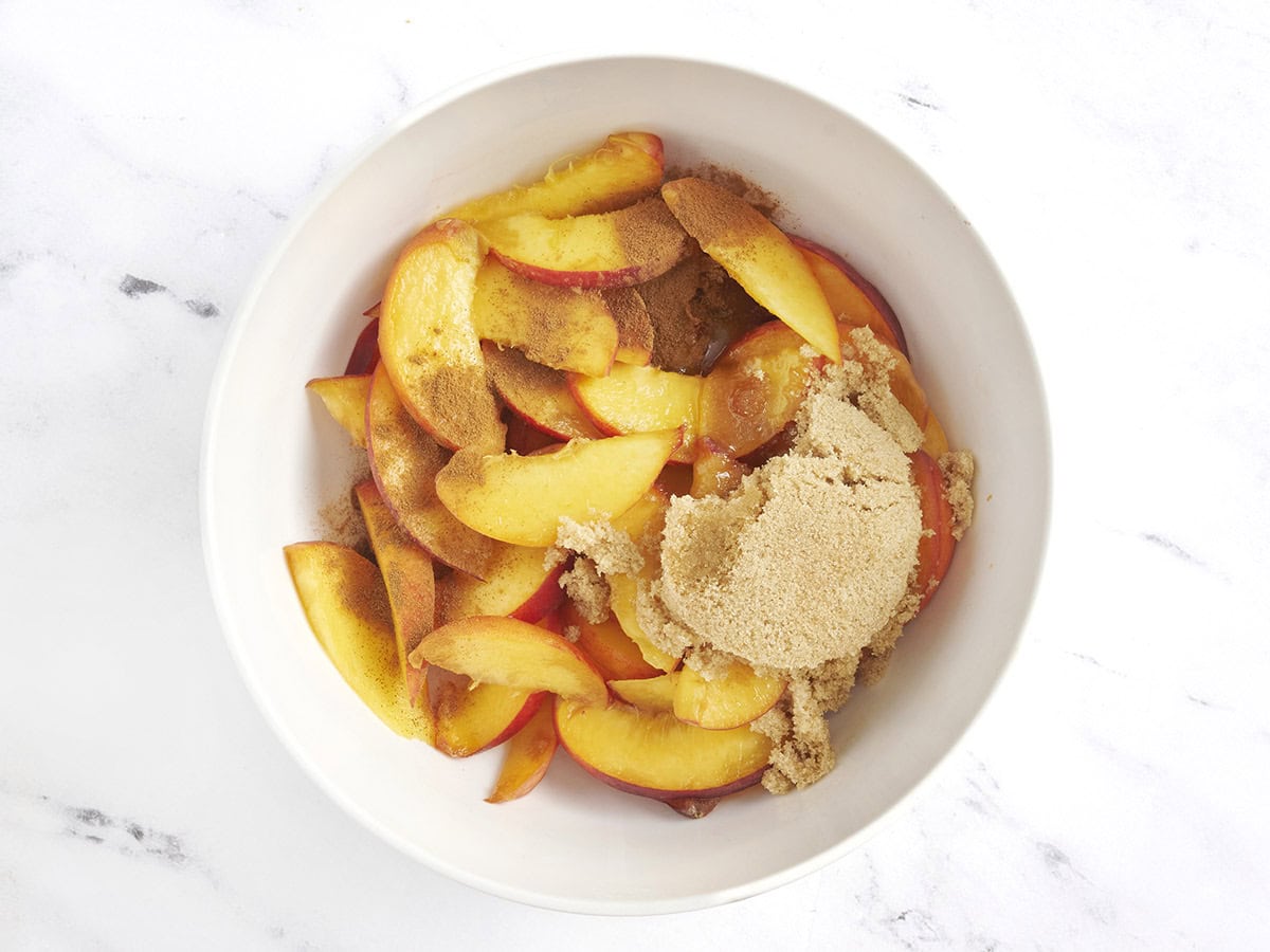 Brauner Zucker und Zimt zu frischen Pfirsichen in einer Schüssel hinzugefügt.