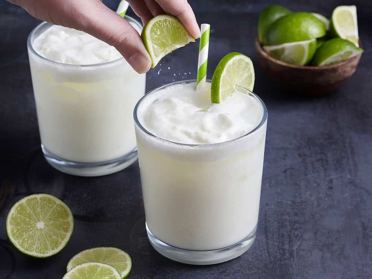 Eine Hand drückt einen Limettenkeil über ein Glas brasilianischer Limonade.