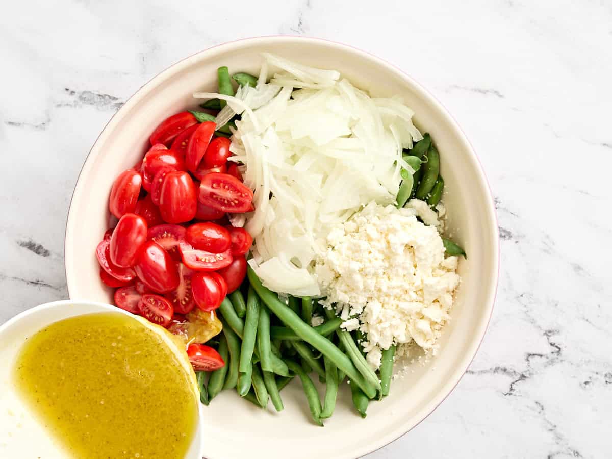 Gehackte Kirschtomaten und Zwiebeln, die einer Schüssel blanchierter grüner Bohnen hinzugefügt wurden.