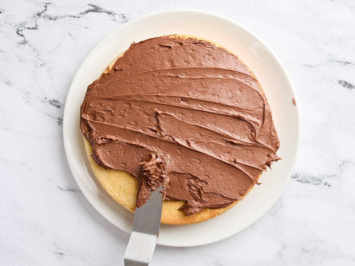 Schokoladenbuttercreme wird auf eine Schicht eines hausgemachten Vanillekuchens ausgebreitet.