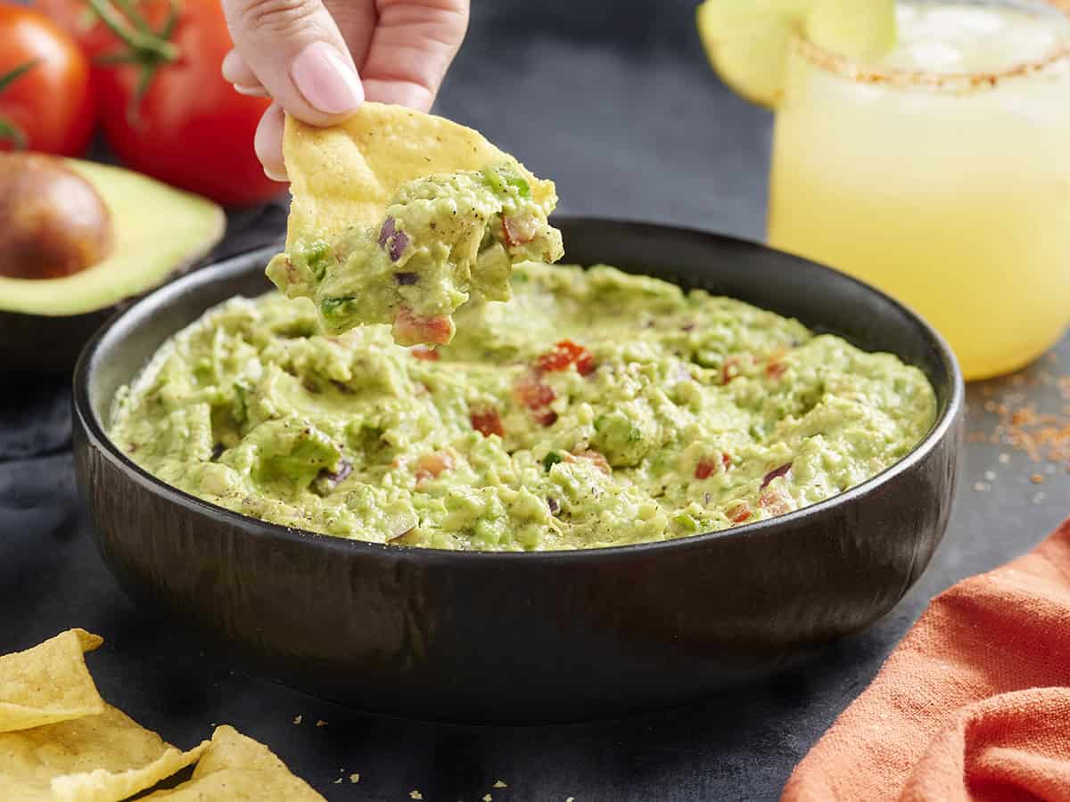 Seitenansicht einer Schüssel Guacamole mit einer Hand, die einen Chip eintaucht.