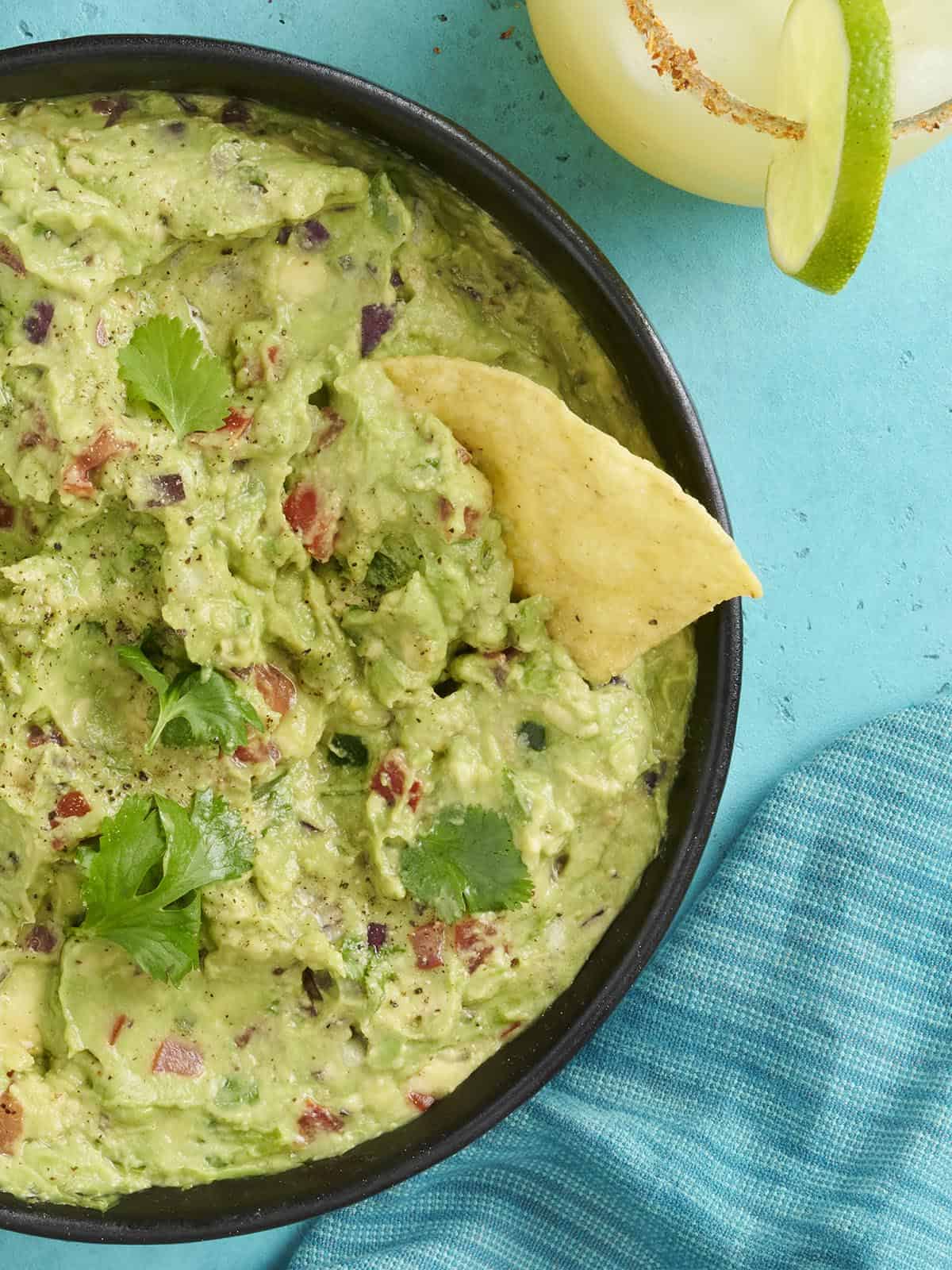 Overhead Nahaufsicht einer Schüssel Guacamole mit einem darin getauchten Chip.