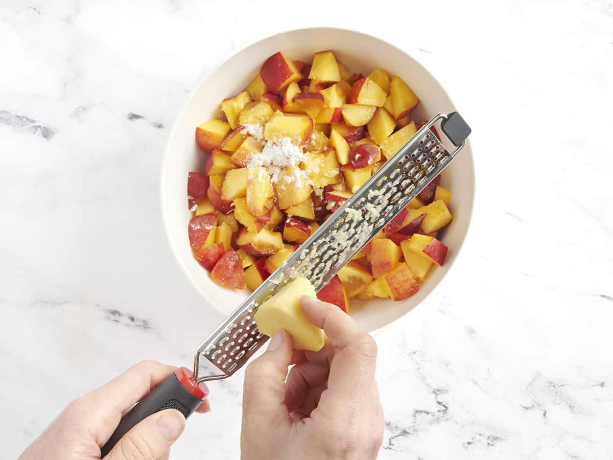 Ingwer wird in eine Schüssel mit Pfirsichscheiben und Maisstärke gerieben.