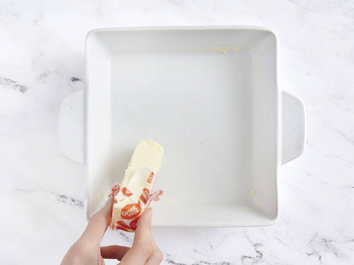 Hände mit einem Butterstab, um eine Auflaufform zu fetten.