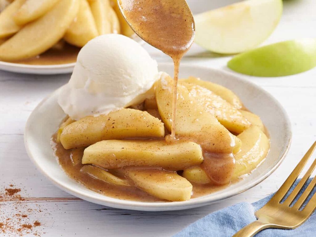 Side view of fried apples on a plate with vanilla ice cream and syrup being drizzled on top.