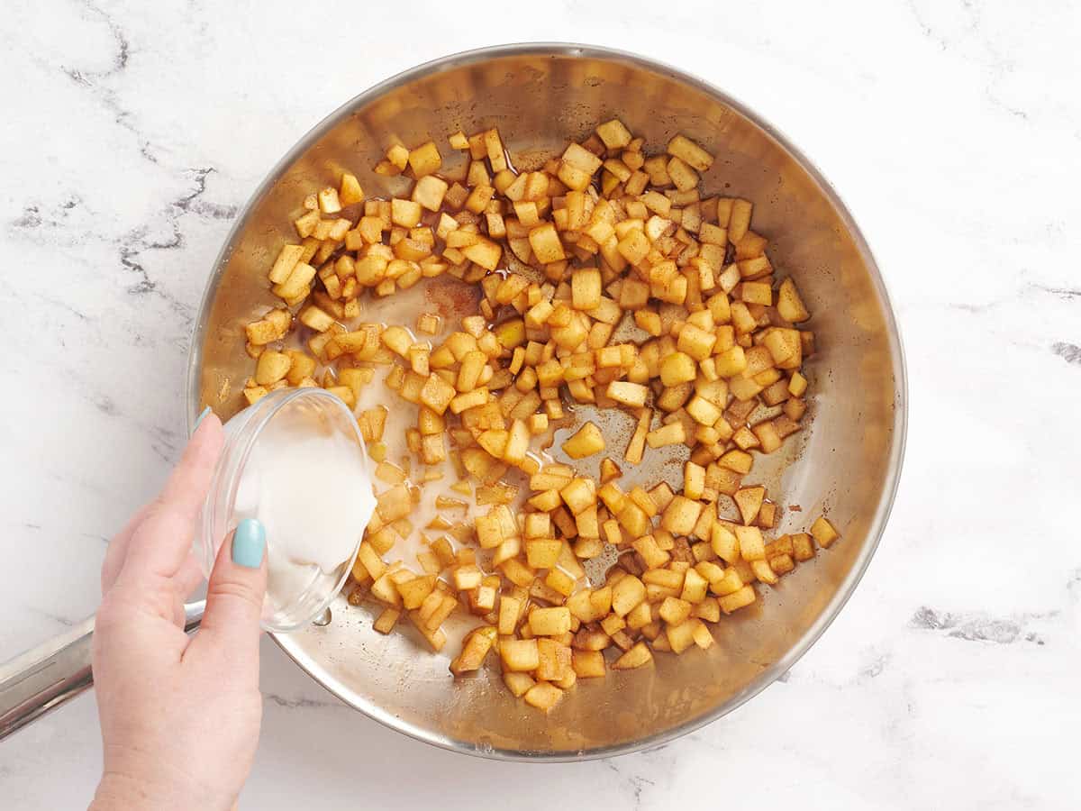 Eine Maisstärdeschlitzung, die in eine Pfanne mit weichem gewürfeltem Apfel gegossen wird.