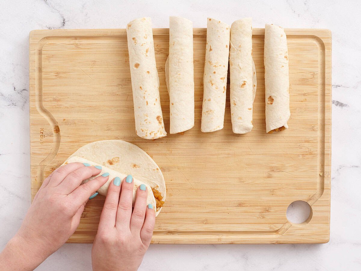 Hände rollen eine Mehl -Tortilla hoch, um eine hausgemachte Apfelflauta zu machen.