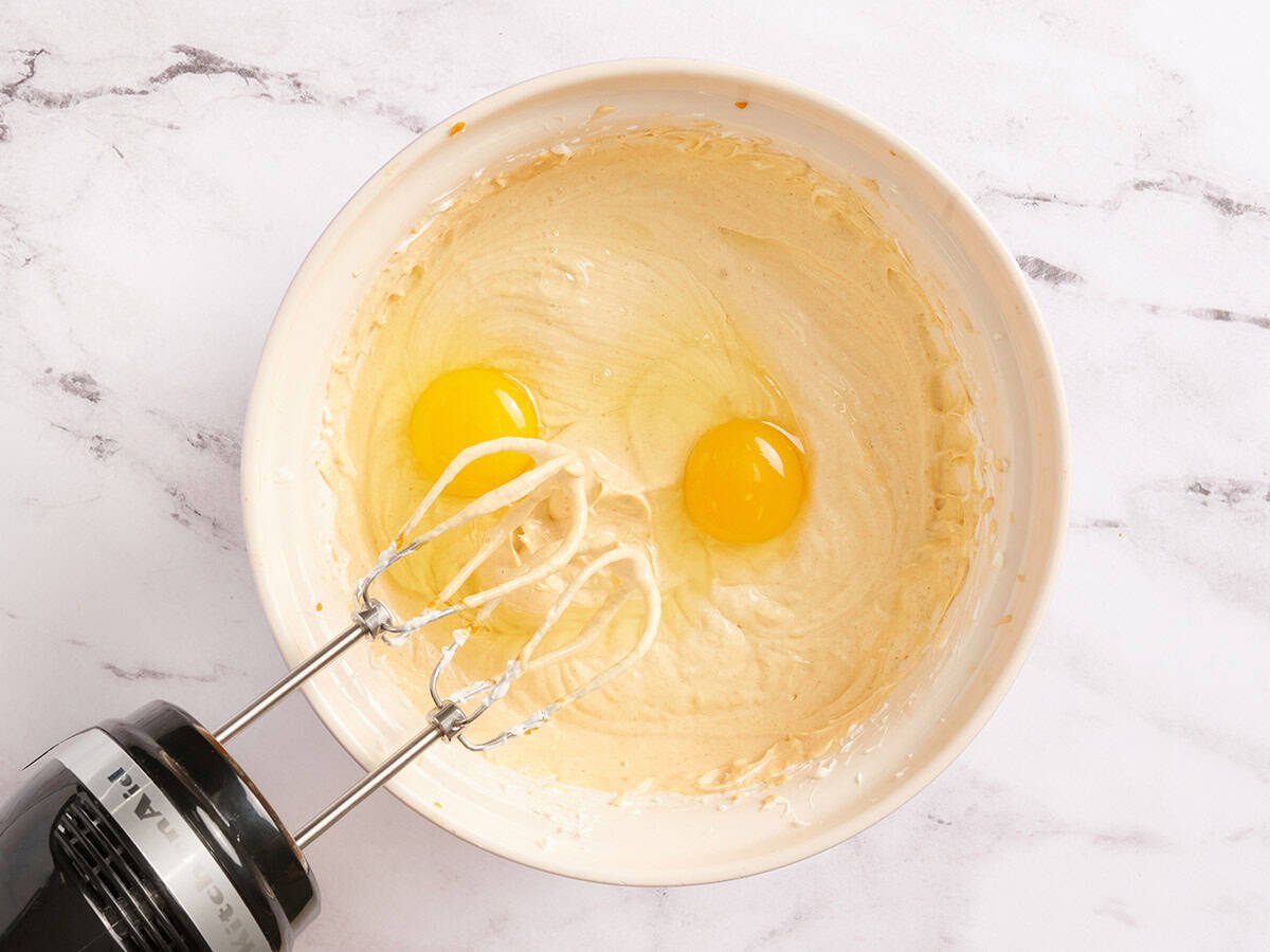 Eier werden zu einer Kürbis-Käsekuchen-Füllung in einer Schüssel hinzugefügt.