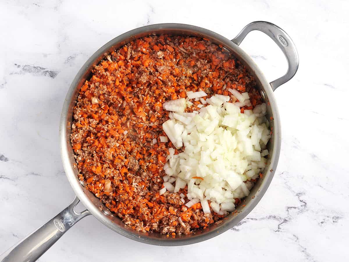 Verarbeitete Karotten, Pilze und Zwiebeln in einem Topf.