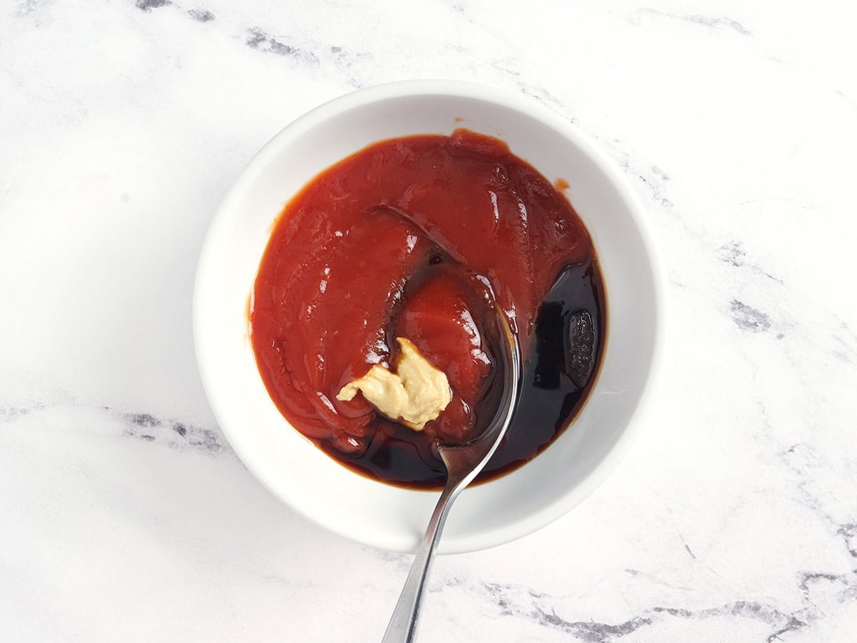 Dijon-Senf, Ketchup, Sojasauce und brauner Zucker werden mit einem Löffel in einer Schüssel vermischt.