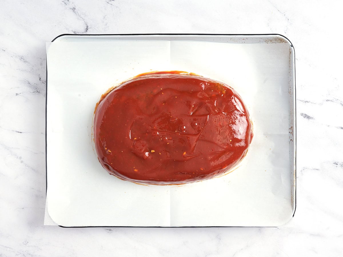 Ein Linsenhackbraten auf einem mit Backpapier ausgelegten Backblech mit Glasur.