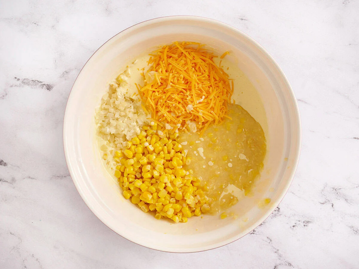 Dosenmais, Käse und Zwiebeln in die Joghurt-/Eierschüssel geben.