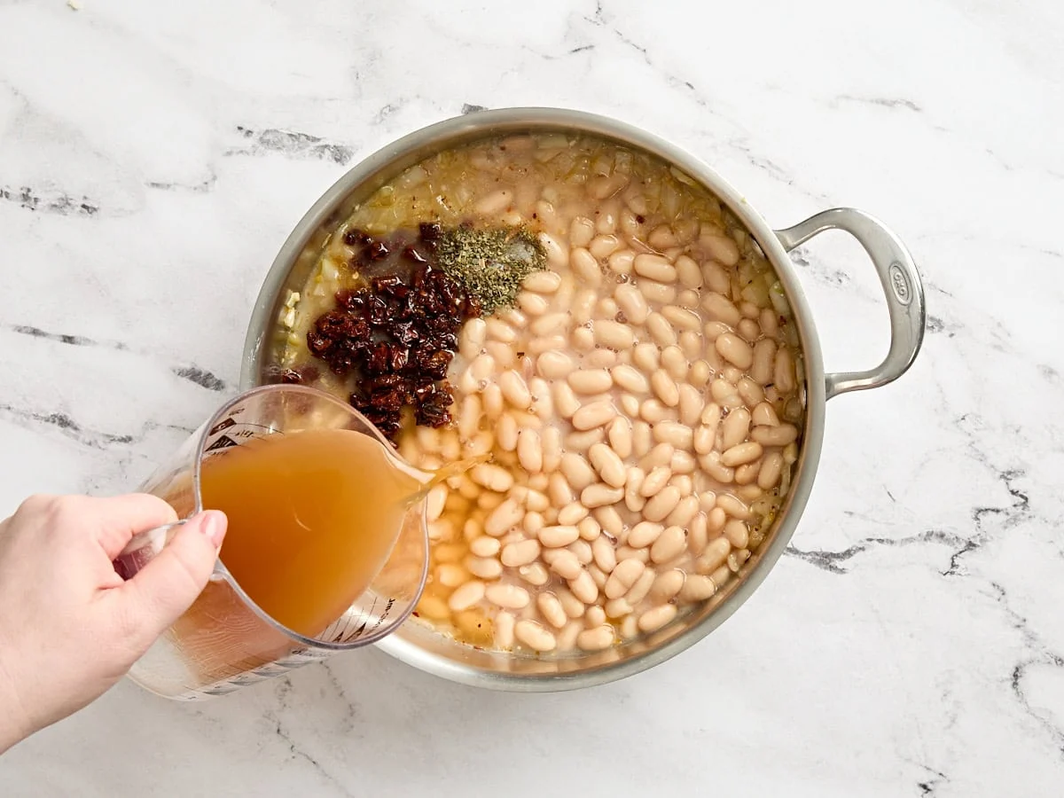 Weiße Bohnen in einer Pfanne mit Gewürzen und Brühe vermischen.