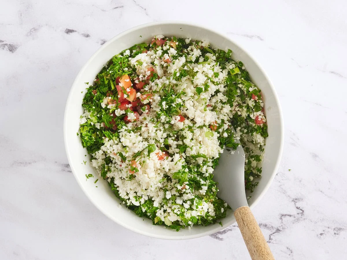 Ein Spatel, der ein Blumenkohl-Tabouleh in einer Schüssel faltet.
