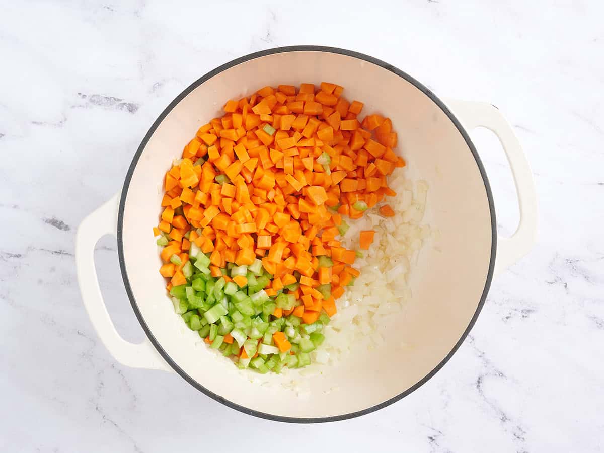 Karotten und Sellerie zu den Zwiebeln in einer Pfanne hinzufügen.