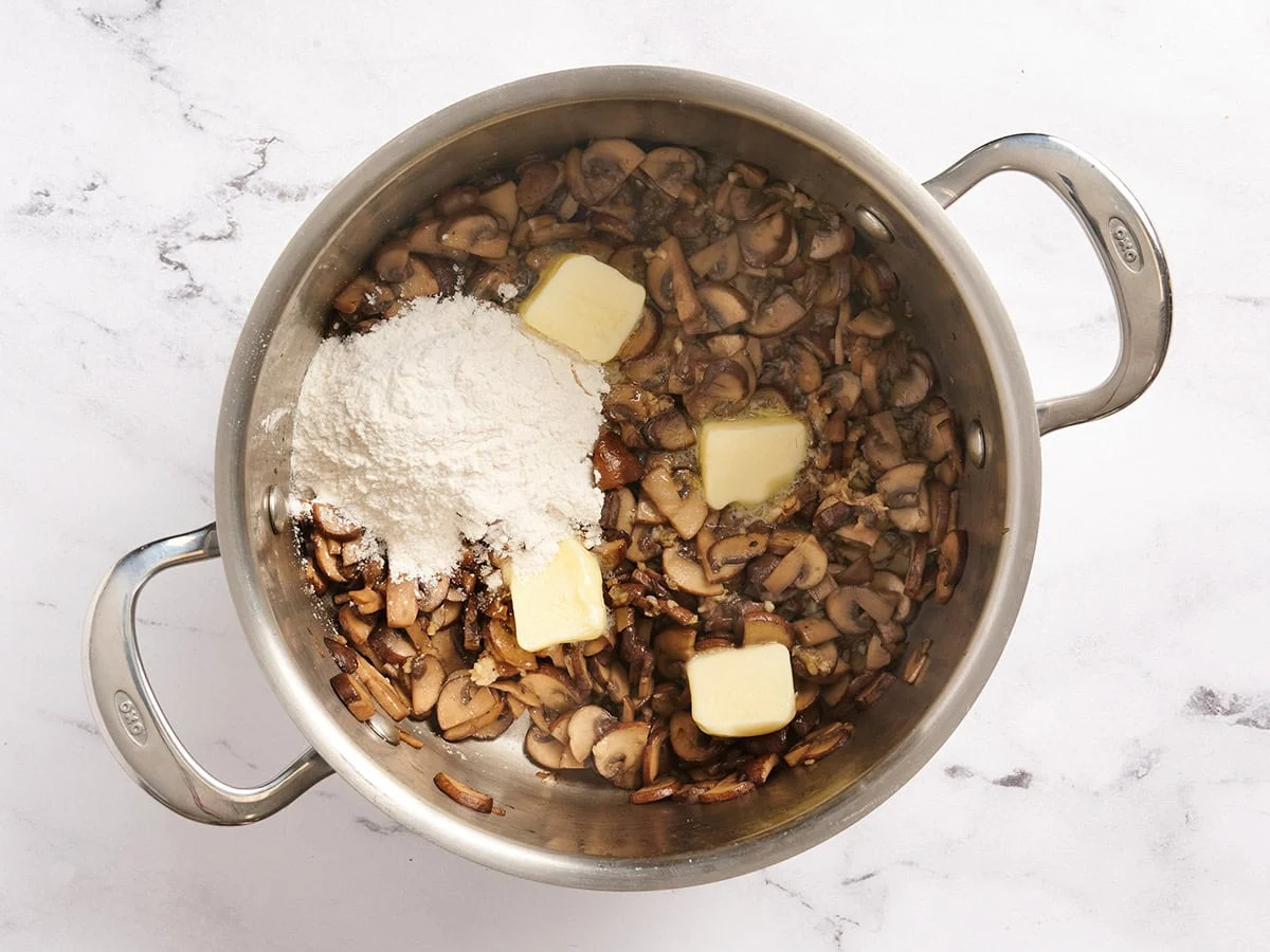 Butter und Mehl in eine Pfanne mit sautierten Pilzen geben.