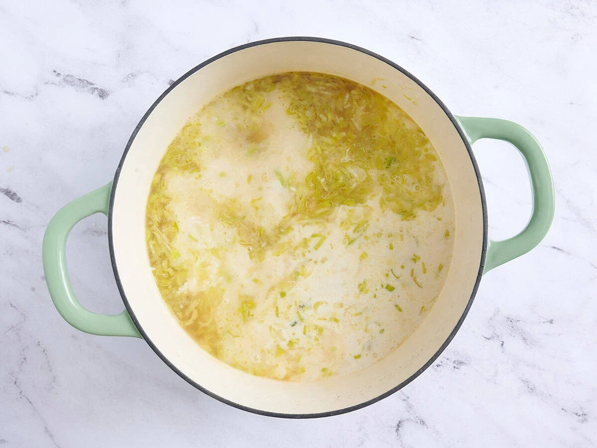 In einem Topf temperierte Sahne zur Kartoffel-Lauch-Suppe hinzufügen.