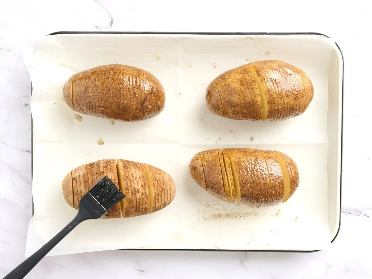 Hasselback-Kartoffeln werden mit gewürztem Öl bestrichen.