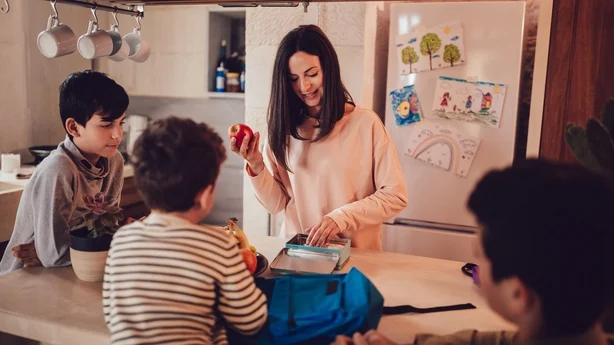 Mutter bereitet Lunchpakete mit gesundem Essen und Snacks für Söhne vor, bevor sie zur Schule gehen