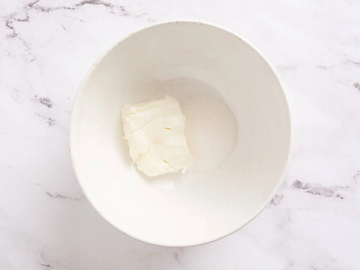 Zucker und Frischkäse in eine Rührschüssel geben.