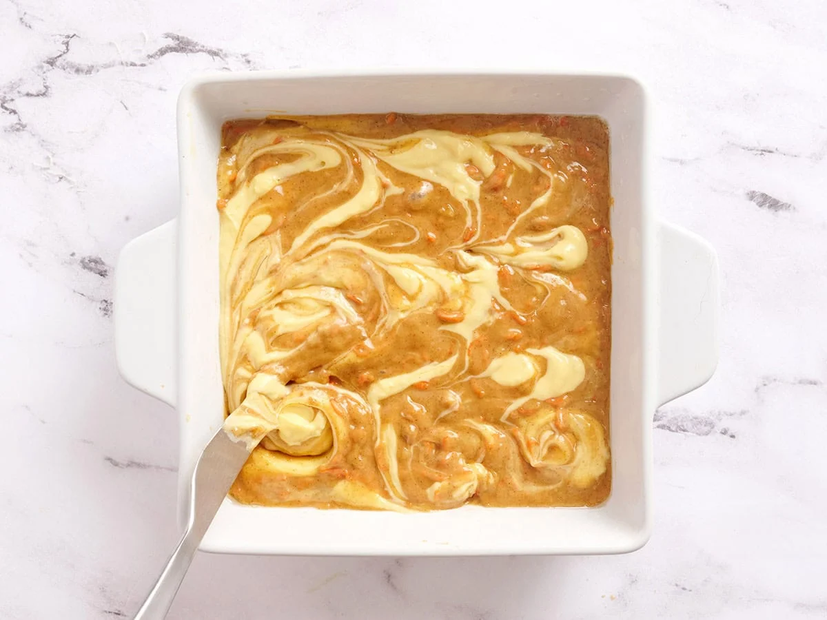 Käsekuchen wirbelt auf Karottenkuchenriegeln in einer Auflaufform.