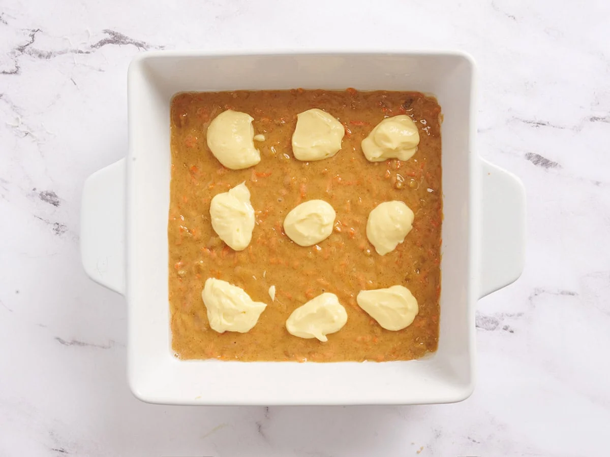 Eine Schicht Karottenkuchen-Riegelmischung in eine Auflaufform geben und Käsekuchenmischung darauf verteilen.