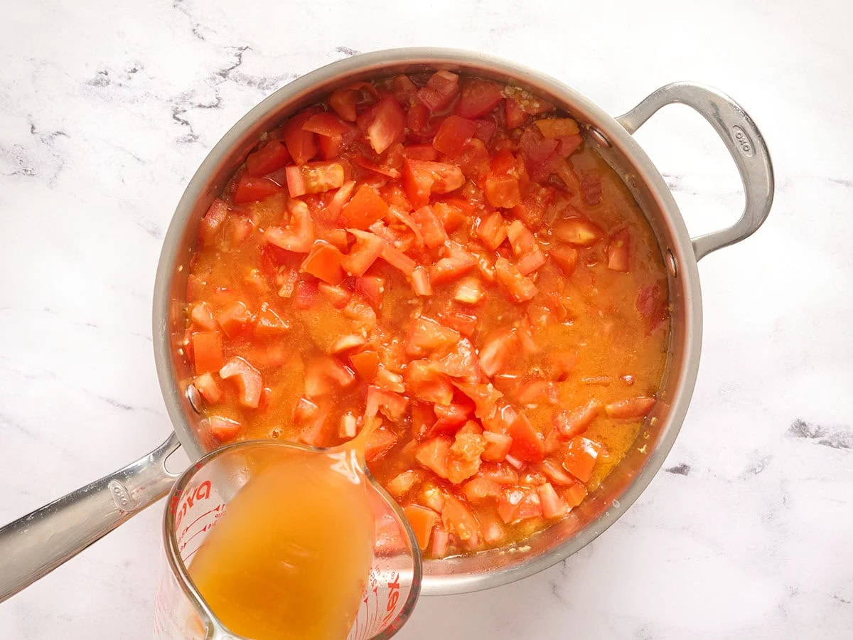 Brühe zu den Tomaten in einer Pfanne geben.