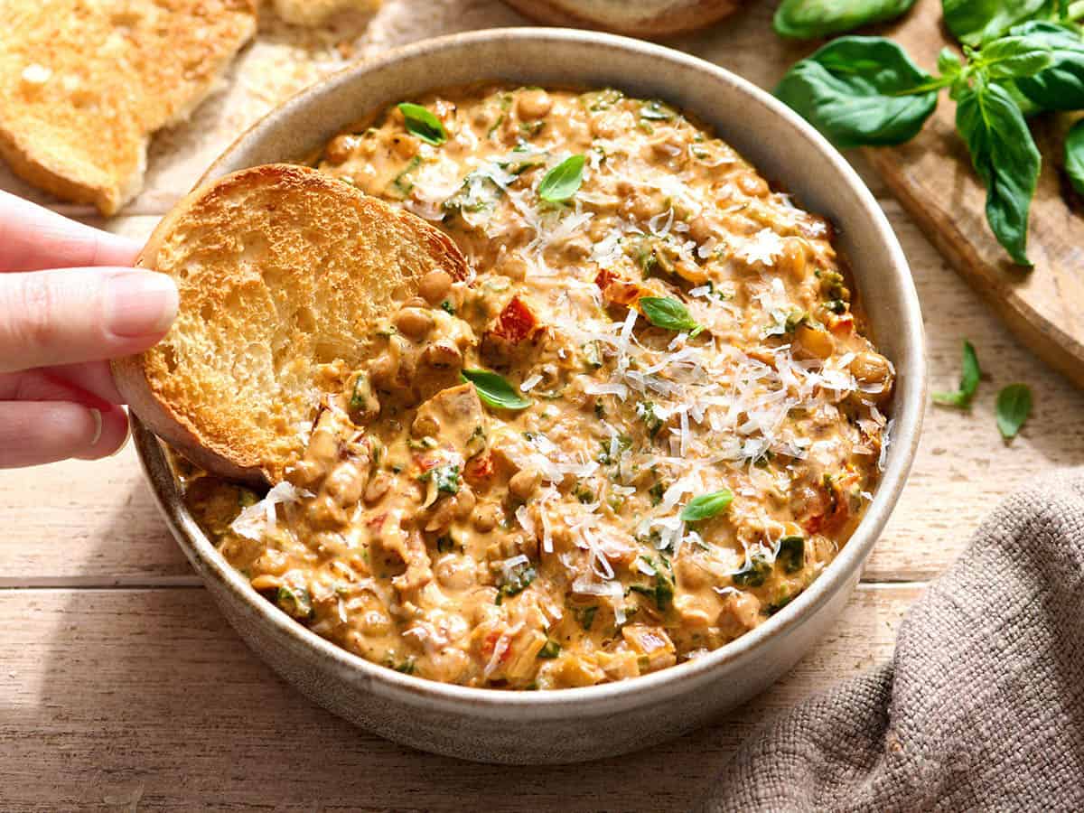 Eine Hand taucht eine Scheibe geröstetes Brot in eine Schüssel mit „Marry Me“-Linsen.