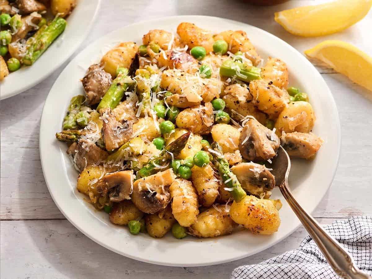 Ein Teller mit Frühlingsgemüse-Gnocchi auf einem Teller mit einer Gabel.