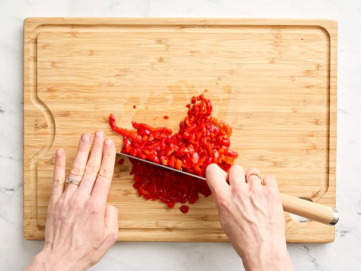 Hände zerkleinern Pimentpaprika mit einem Messer.
