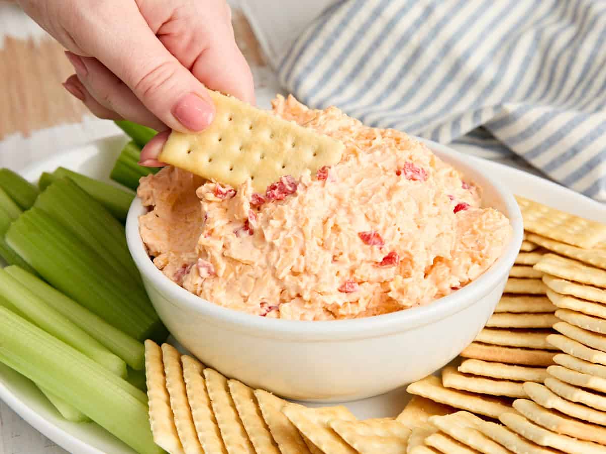 Seitenansicht einer Schüssel mit Southern-Pimento-Käse-Dip, in die eine Hand einen Cracker eintaucht.