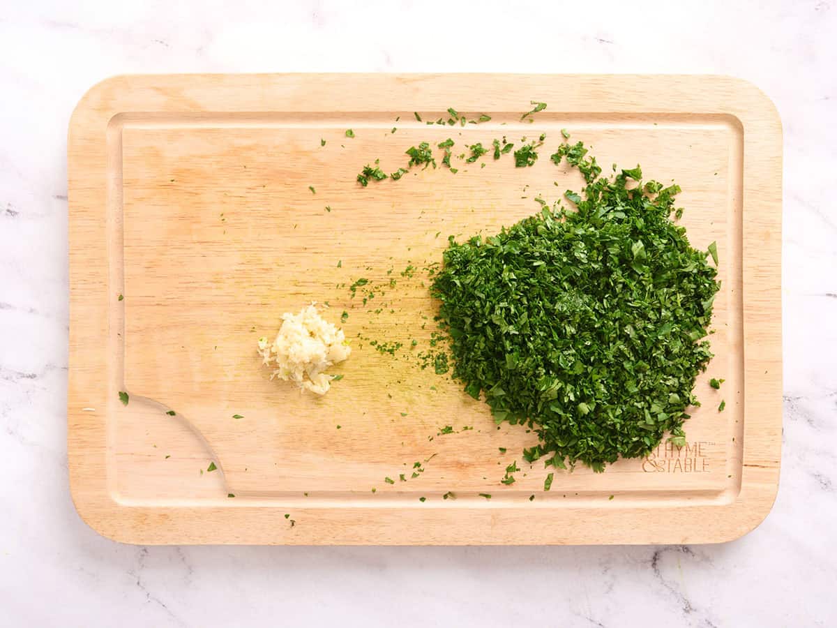 Gehackte Kräuter und gehackter Knoblauch auf einem Schneidebrett.