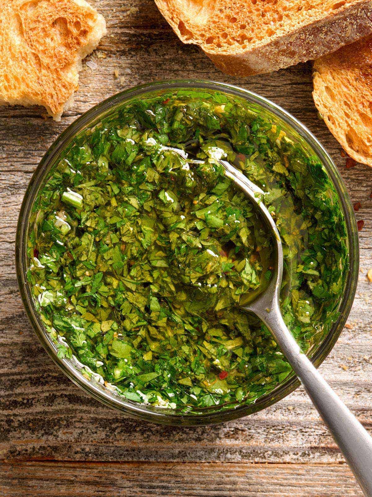 Chimichurri-Sauce ist eine würzige, frische und Knoblauchsauce, die jeder Mahlzeit einen tollen Geschmack verleiht. Als Marinade, Dip-Sauce oder Gewürz verwenden. Budgetbytes.com Draufsicht auf eine Schüssel Chimichurri-Sauce mit einem Löffel.