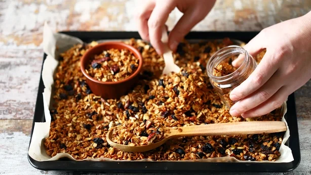 Frisch zubereitetes hausgemachtes Müsli auf einem Backblech. Granola in einem Holzlöffel und in einem Glas. Selektiver Fokus. Gesundes Ernährungskonzept. Keto-Diät.