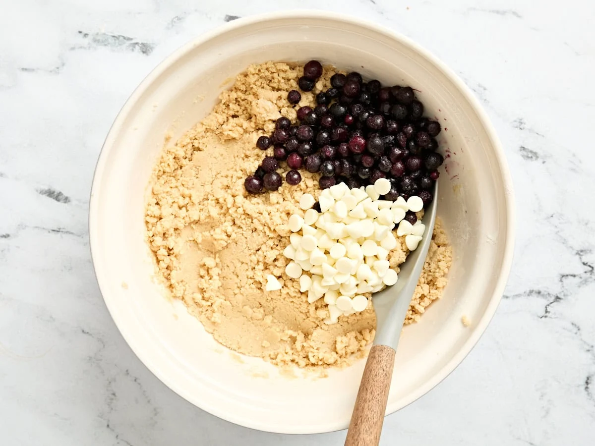 Blaubeeren und weiße Schokoladenstückchen in eine Schüssel mit Keksteig geben.