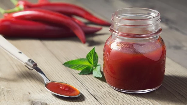 Porträt von roten Chilischoten-Konfitüre, die auf einem Teelöffel liegt