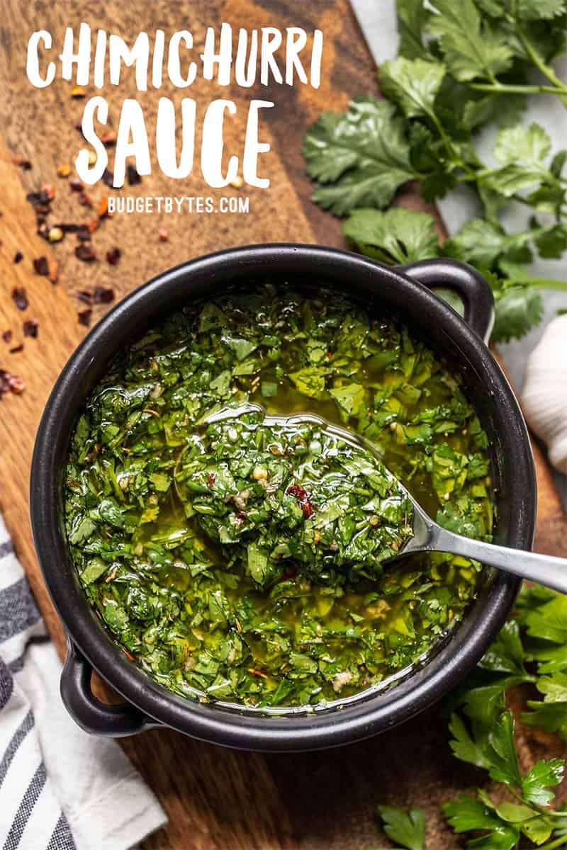 Eine schwarze Schüssel voller Chimichurri-Sauce, aus der ein Löffel etwas heraushebt, Nahaufnahme.