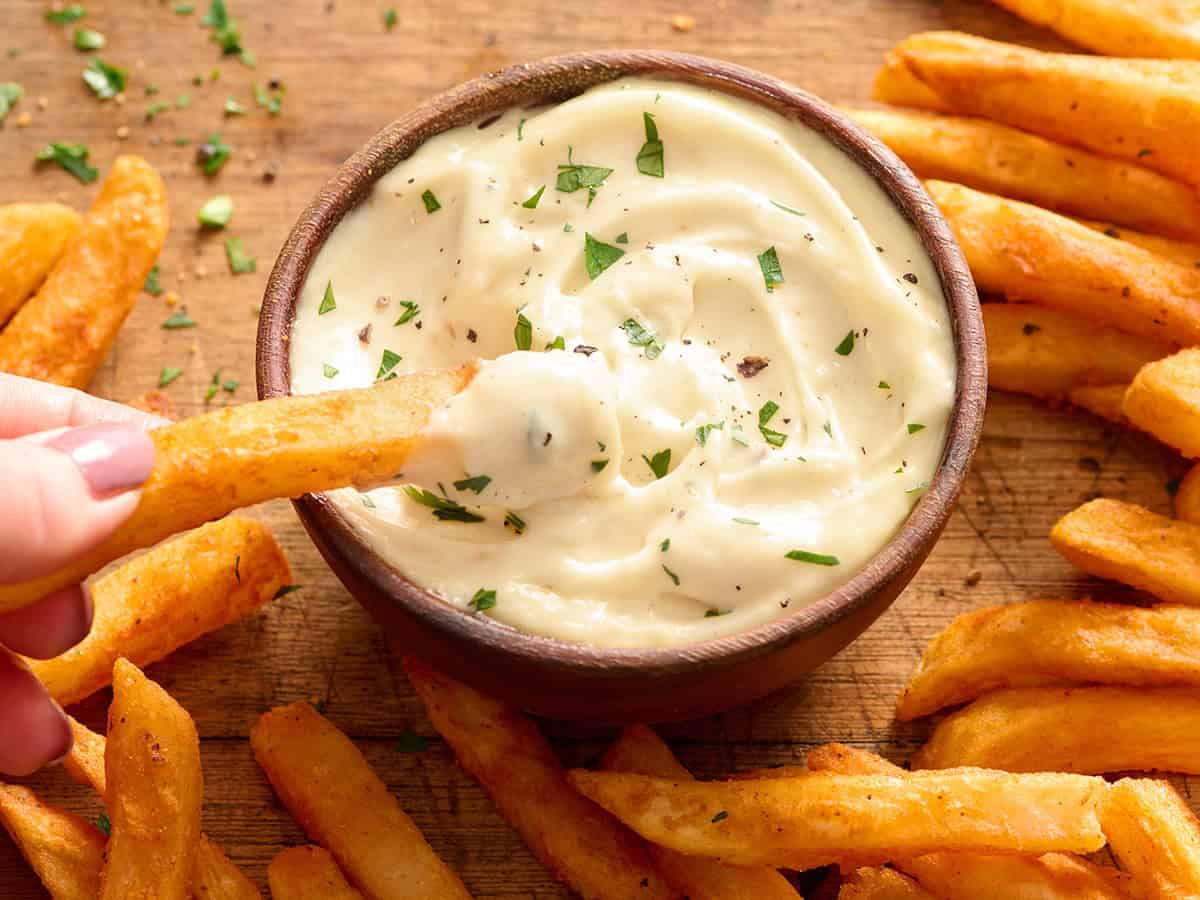 Draufsicht auf eine Schüssel mit hausgemachter Knoblauch-Aioli, in die eine Pommes frites getunkt wird.