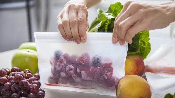 Eine junge Mutter packt gefrorene Himbeeren in einen durchsichtigen Lebensmittelbeutel.