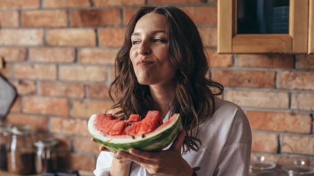 Frau zu Hause isst Wassermelone in der Küche.
