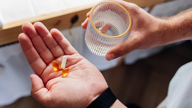 Nahaufnahme einer Person, die sich zu Hause auf die Einnahme von Vitaminpräparaten mit einem Glas Wasser vorbereitet. Tägliches Wohlbefinden, Gesundheitsroutine und Selbstpflegekonzept.