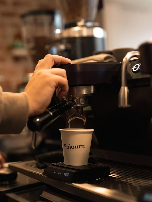 Ein Barista trinkt an einer Kaffeemaschine einen Espresso