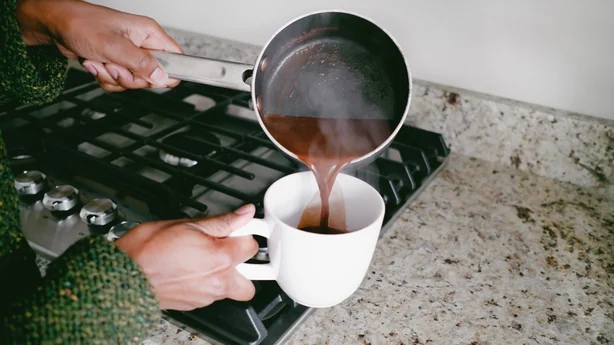 Nahaufnahme einer nicht wiederzuerkennenden schwarzen Frau, die heiße Schokolade in eine Tasse gießt