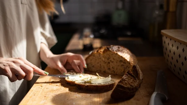 Frau verteilt Butter auf einer Scheibe Vollkornbrot auf einem Holzschneidebrett