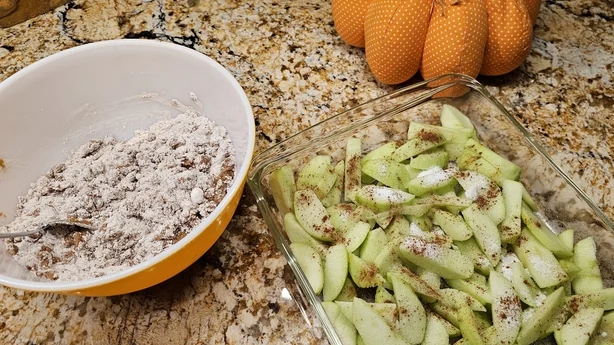 Scheiben von Granny-Smith-Äpfeln zusammen mit Mehl, Muskatnuss und Zimt in einer Schüssel, bereit zum Mischen der Zutaten für ein köstliches Lieblingsdessert der Saison.